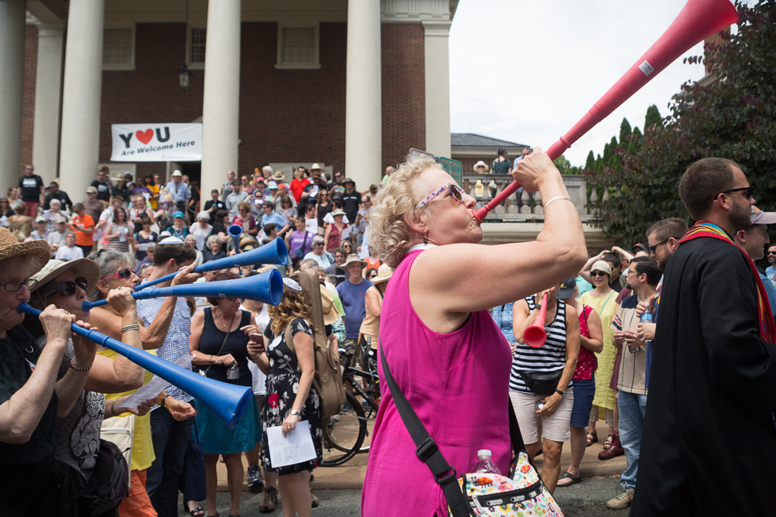 The Rev. Seth Wispelwey (right), co-moderator of Sojourners United Church of Christ in Charlottesville, Va., leads a group headed to oppose a KKK Rally there, as the Rev. Elaine Ellis Thomas, associate rector and chaplain, St. Paul's Memorial Episcopal Church (second from right) blows a vuvuzela. Behind them is First United Methodist Church, where the Charlottesville Clergy Collective had arranged a gathering. An estimated 1,000 were on hand to protest the rally. Photo by Michael Cheuk.