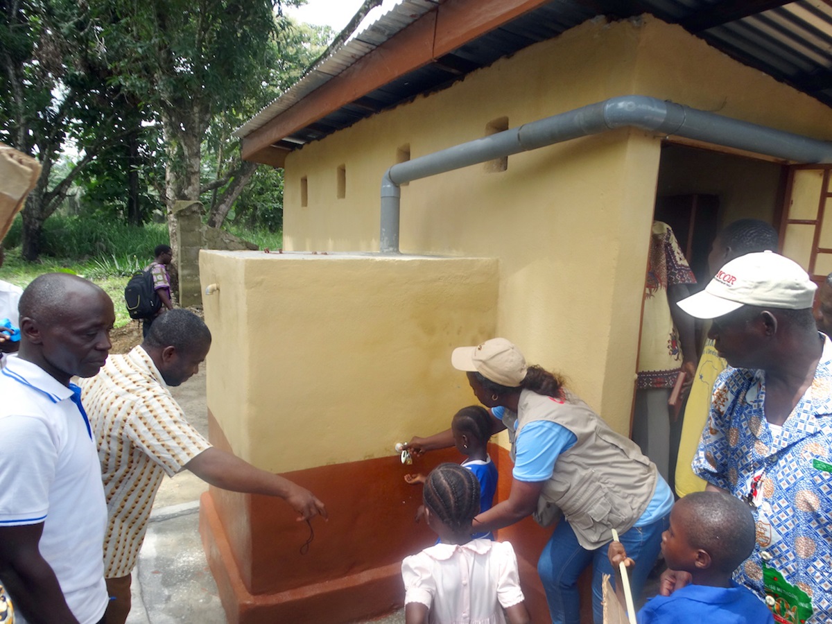 Health Coordinator Catherine Norman (center in cap) shows children of the United Methodist Church Primary School in Fulawahun, Sierra Leone, how to use a water faucet to wash their hands after using the toilet, while Bishop Yambasu (far right) looks on. A United Methodist Global Health agency initiative has provided much needed toilets and wells for primary schools in two rural communities that previously had a prevalence of diarrhea and worm infestations due mainly to lack of toilets and good drinking water. Photo by Phileas Jusu, UMNS. 