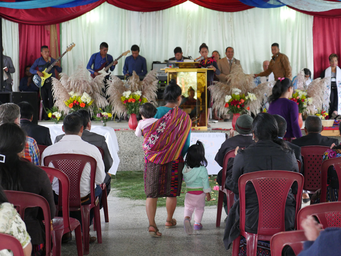 An usher with her two small children prepares to take an offering at Iglesia Nacional Methodista Fuente De Vida, Guatemala.