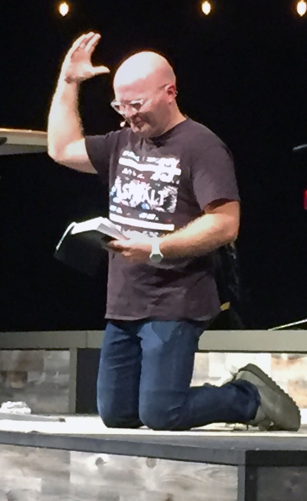 The Rev. Adam Weber, lead pastor of Embrace Church in Sioux Falls, S.D., kneels during his sermon on prayer. Photo by Heather Hahn, UMNS.