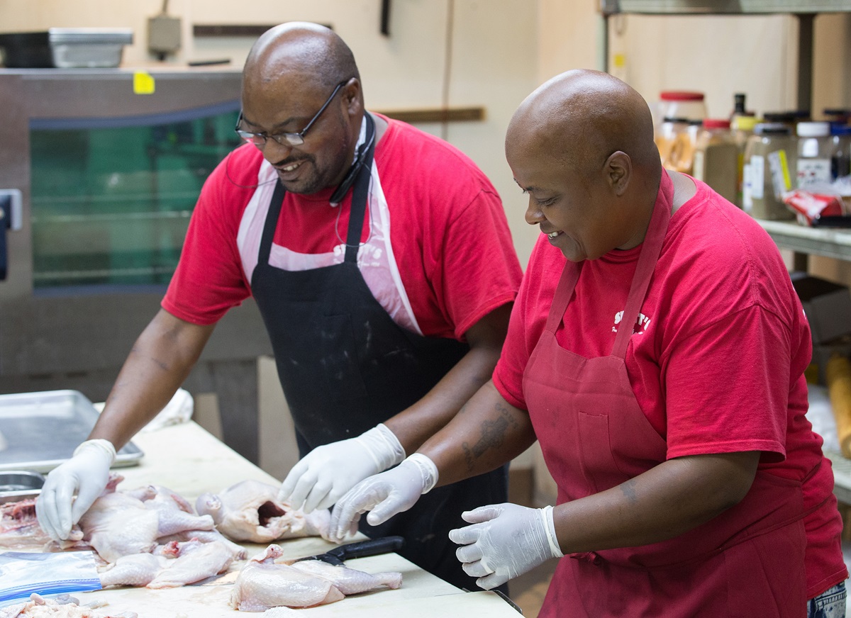 Martin Carter, left, teaches Debra Kelley to cut up chickens in preparation for making jerk chicken. “I enjoy this, cooking so people can come in and get good food,” says Kelley, an ex-offender working at Swett’s restaurant. Photo by Mike DuBose, UMNS.