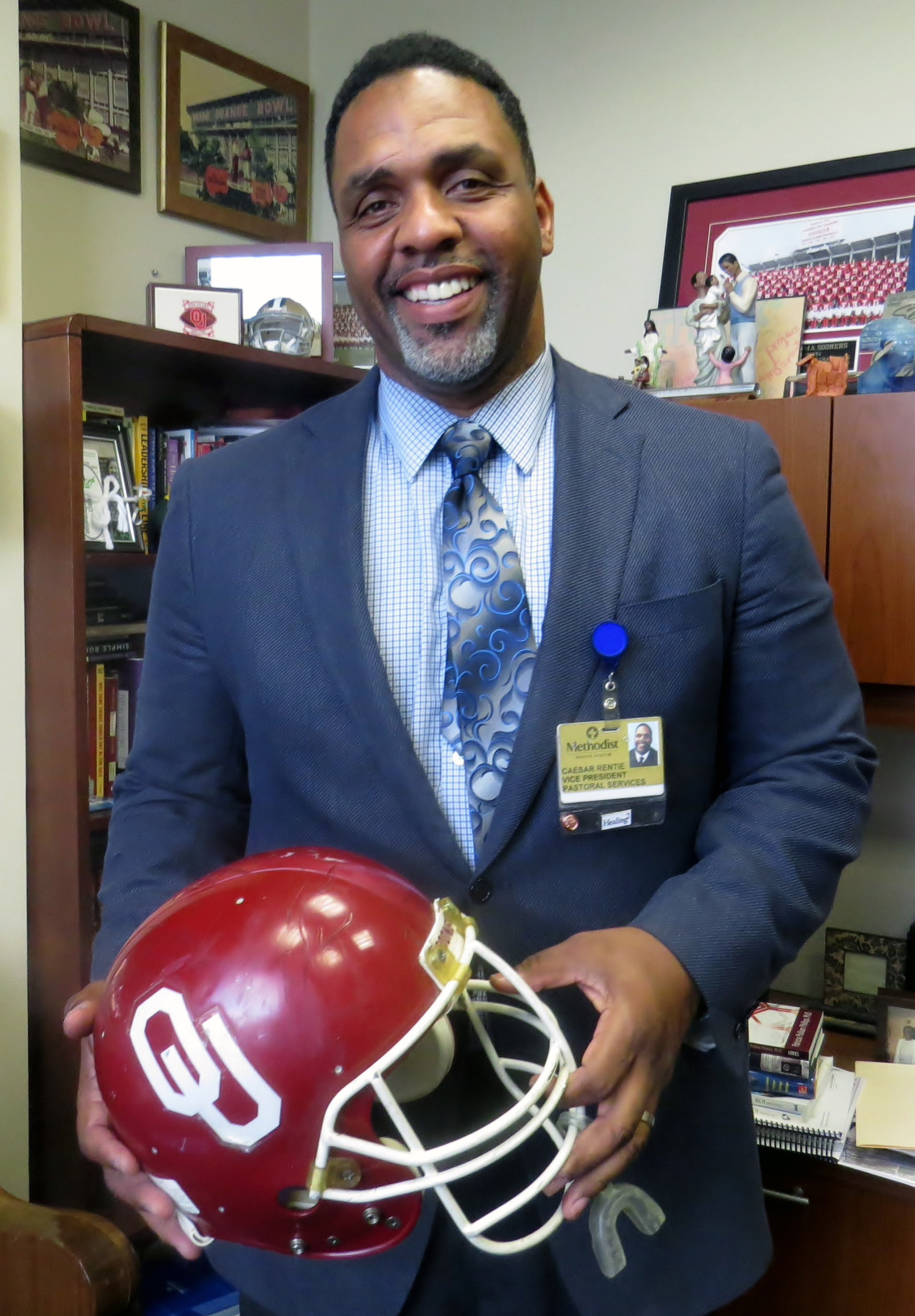 The Rev. Caesar Rentie, vice president for pastoral services at Methodist Health System in Dallas, holds a helmet from his days as an offensive tackle for the Oklahoma Sooners. Rentie likes to say he’s available for counseling to University of Texas fans whenever their school has to play Oklahoma. Photo by Sam Hodges, UMNS.
