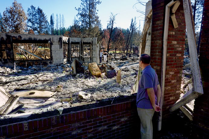 The Rev. Blake Busick looks through an opening at his house at rubble and singed trees after wildfires swept through his neighborhood in Santa Rosa, California. Photo by Sue Larson, courtesy of the Rev. Blake Busick.