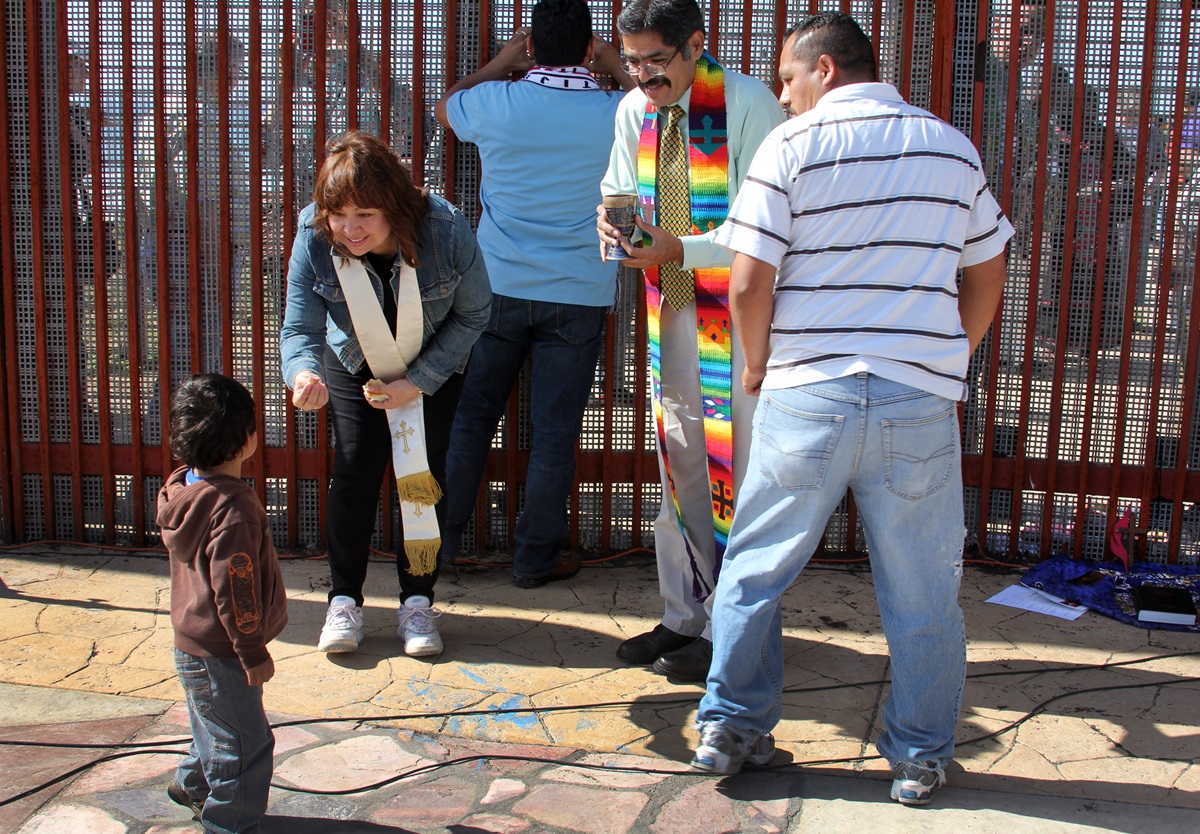 Bishop Minerva G. Carcaño shares communion bread with a little boy and his father in El Faro Park at the U.S./Mexico border. To her right is Pastor Felipe Ruiz Aguilar. 2013 file photo by Kathleen Barry, UMNS.
