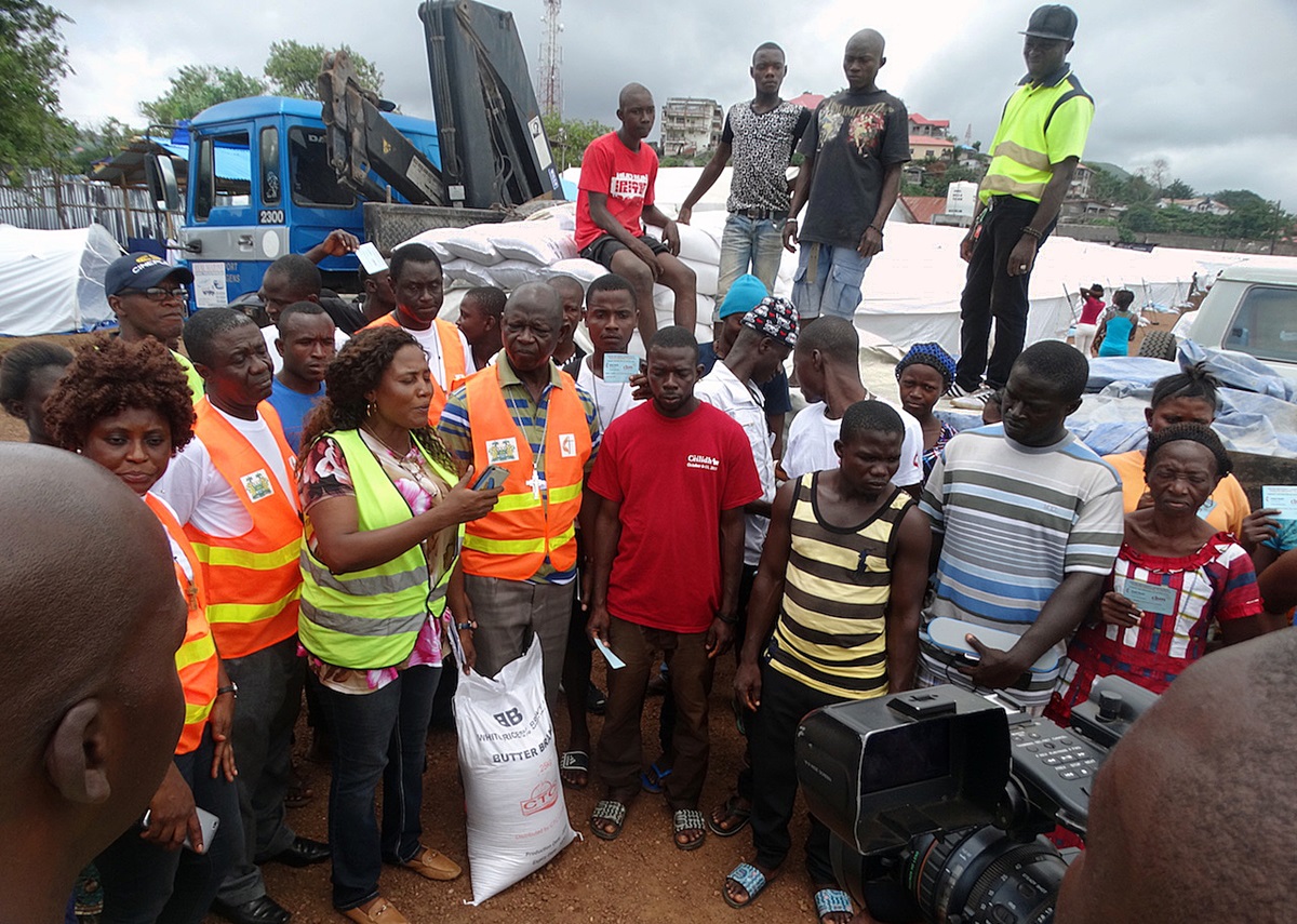 At Juba Camp in Freetown, Sierra Leone, Bishop John Yambasu (fourth from left, front row) leads a symbolic handing over of 200 bags of rice to the Office of National Security, the government agency in charge of coordinating welfare matters for survivors of deadly mudslide Aug. 14. Because survivors are not allowed to cook in their temporary plastic-cover homes, the ONS hires people to prepare food for them three times a day. Photo by Phileas Jusu, UMNS.