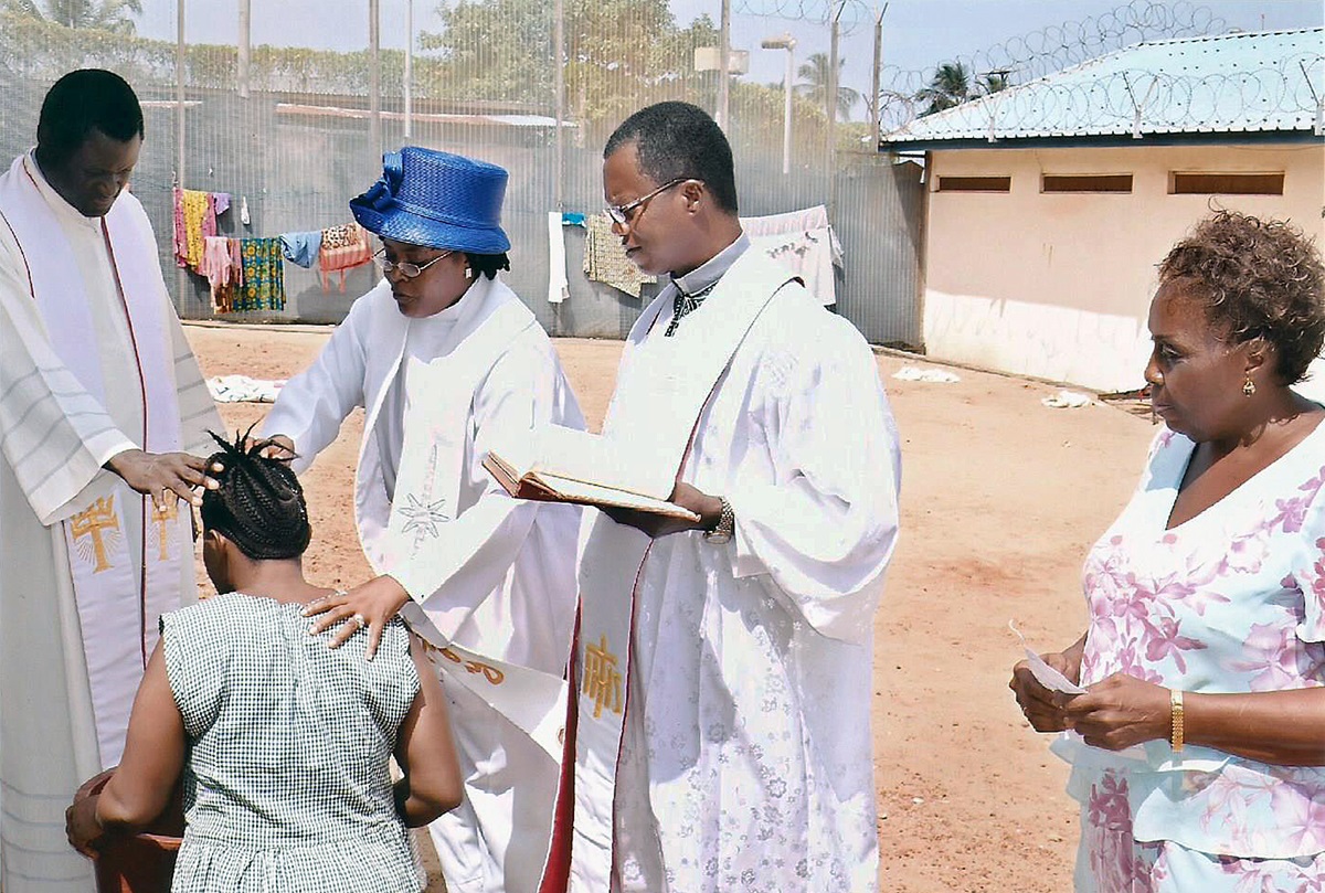 The Rev. Daisy Gbloh (center, standing), supported by the Rev. Winston Ashcroft and the Rev. Alex Josiah, baptizes a woman at the Female Correctional Center in Freetown, Sierra Leone. Photo by Phileas Jusu, UMNS.