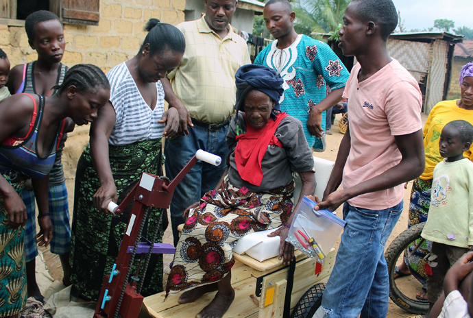 Mother Yei Sendolo, 80, is helped into her Personal Energy Transportation vehicle while family members look on. Photo by Julu Swen, UMNS.