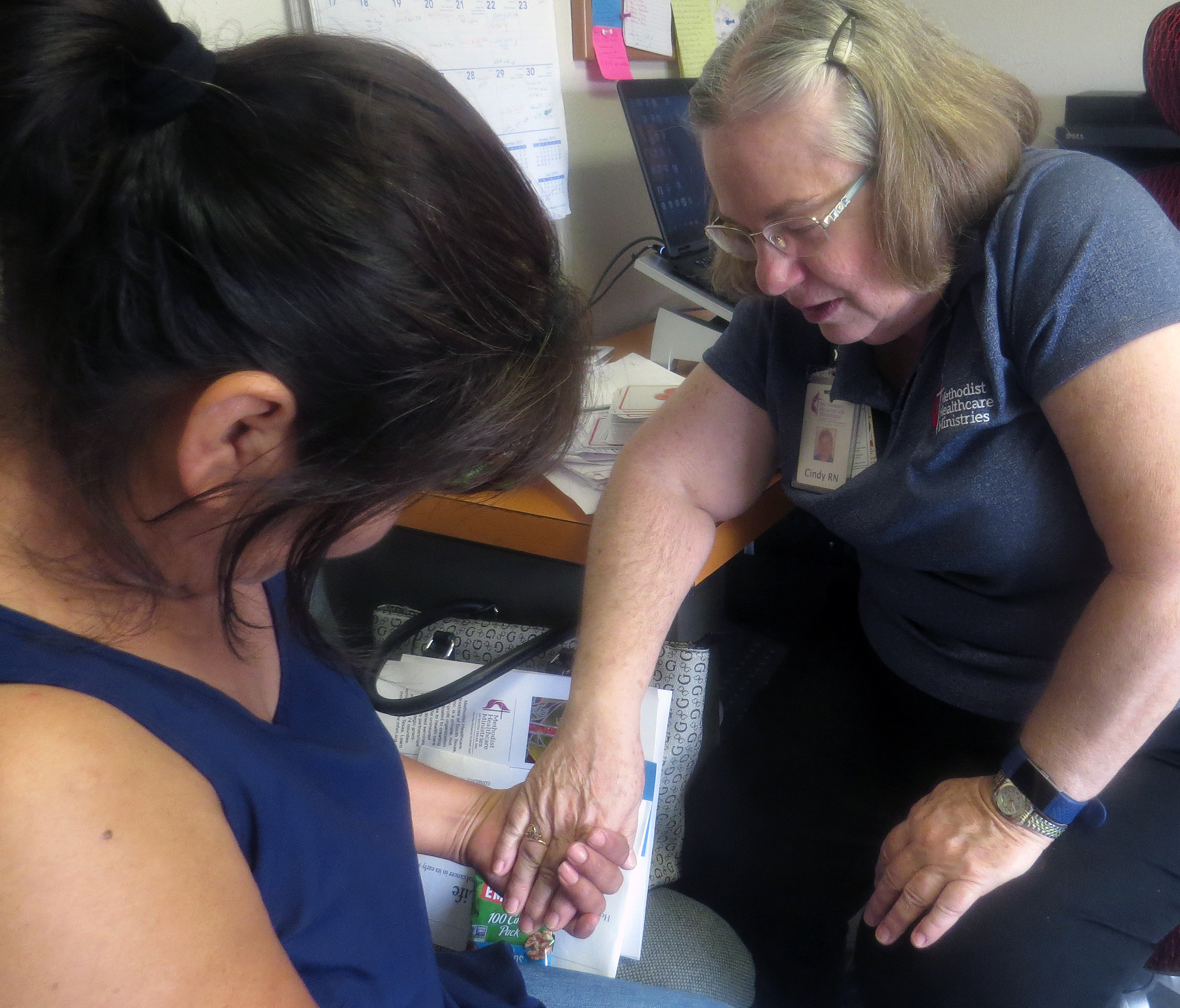 Cindy Bishop, Wesley Nurse, prays with Patricia Pesina in Bishop’s office at First United Methodist Church in Edinburg, Texas. Bishop has been working to get Pesina a set of dentures. Wesley Nurses do public health outreach and are based in United Methodist churches  by Methodist Healthcare Ministries of South Texas. Photo by Sam Hodges, UMNS.