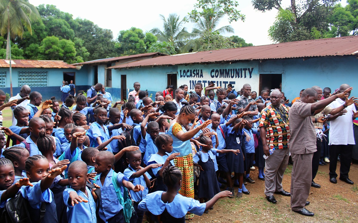 Students, teachers and other adults reach out their hands in prayer toward a new toilet facility during a dedication at LACOSHA Community Institute in the Pipeline Community, in Paynesville, Liberia. The dedication was part of activities marking World Toilet Day by the United Methodist Church in Liberia. Photo by Julu Swen, UMNS.