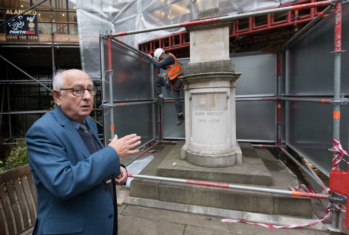 Tour guide Allen Steel points out John Wesley's tomb in the garden at Wesley's Chapel while a worker climbs down from scaffolding erected to protect the historic site from encroaching construction in the area that has become known as the “silicon roundabout” because of the presence of high-tech industries. Photo by Mike DuBose, UMNS.