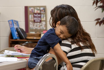 A DACA applicant cradles her son as she fills out the many pages of paperwork required by Immigration and Customs Enforcement.