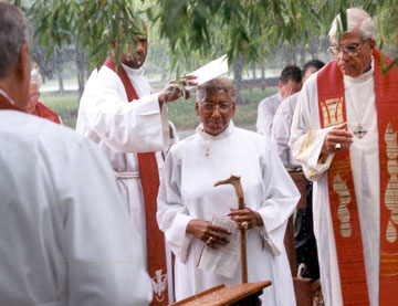 Alfred Johnson (left) tries to keep the rain out of the Rev. Violet L. Fisher's face during her service of consecration as a bishop in Somerset, N.J., in 2000. To her right is Bishop George W. Bashore. A UMNS photo by Dean Snyder.