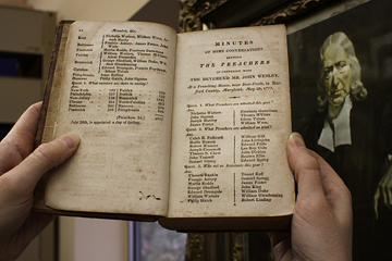 Frances Lyons-Bristol, archivist records administrator, holds a book listing early Methodists, just one of thousands of historic items housed at the denomination's Commission on Archives and History on the campus of Drew University in Madison, N.J. A portrait of the Rev. John Wesley hangs in the background. A UMNS photo by Kathleen Barry.