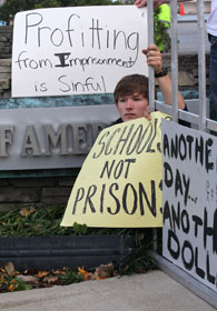 A young adult protests corporate profit from incarceration.