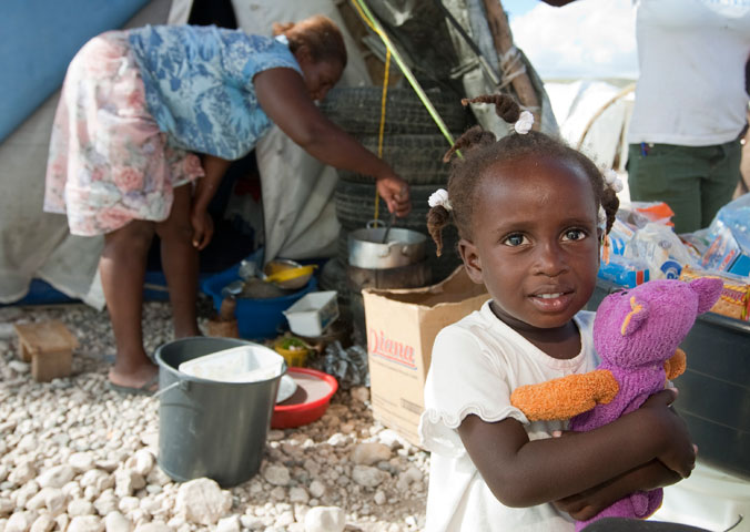 Jeandline, 2, plays with a doll while her mother, Jean Marise, prepares dinner in front of their tent at Camp Corail.