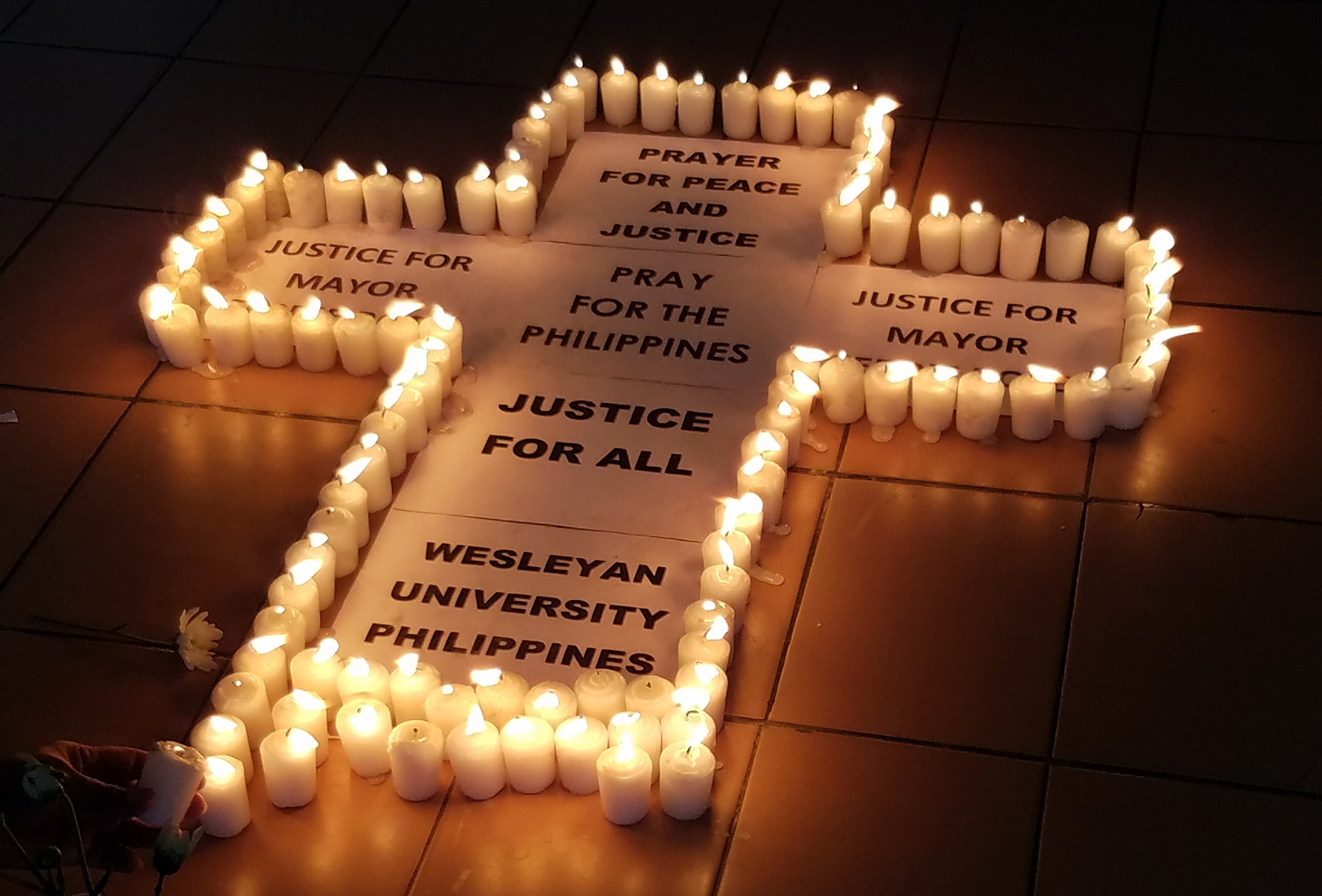 A cross with candles calls for justice and peace at a prayer vigil led by the Rev. Francis Fajardo at Wesleyan University-Philippines for slain mayor, Ferdinand Bote. Bote, mayor of the General Tinio in Nueva Ecija province, was gunned down July 3. Photo courtesy of Clarafe Gonzales & Sergio Arevalo.