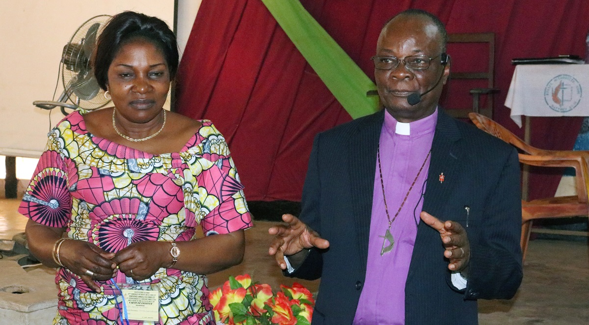Bishop Gabriel Yemba Unda (right), with wife Marie Claire Unda, speaks during the 2018 East Congo Annual Conference in Kindu. Bishop Unda launched an initiative to rebuild United Methodist buildings in the Eastern Congo Episcopal Area after civil wars there destroyed many churches and other structures. Photo by Chadrack Tambwe Londe, UMNS. Bishop Gabriel Yemba Unda (right), with wife Marie Claire Unda, speaks during the 2018 East Congo Annual Conference in Kindu. Bishop Unda launched an initiative to rebuild United Methodist buildings in the Eastern Congo Episcopal Area after civil wars there destroyed many churches and other structures. Photo by Chadrack Tambwe Londe, UMNS.