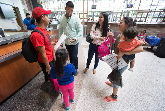 Volunteers César Mata (left, rear) and Maria Peña (right, rear) help Honduran immigrants Isaác Rivera Ramos (left) and his daughter Katerin and Ana Merced Maldonado (right) and her daughter Ashley find the right bus in McAllen, Texas. A monitoring device is visible on Maldonado's left ankle. Photo by Mike DuBose, UMNS.
