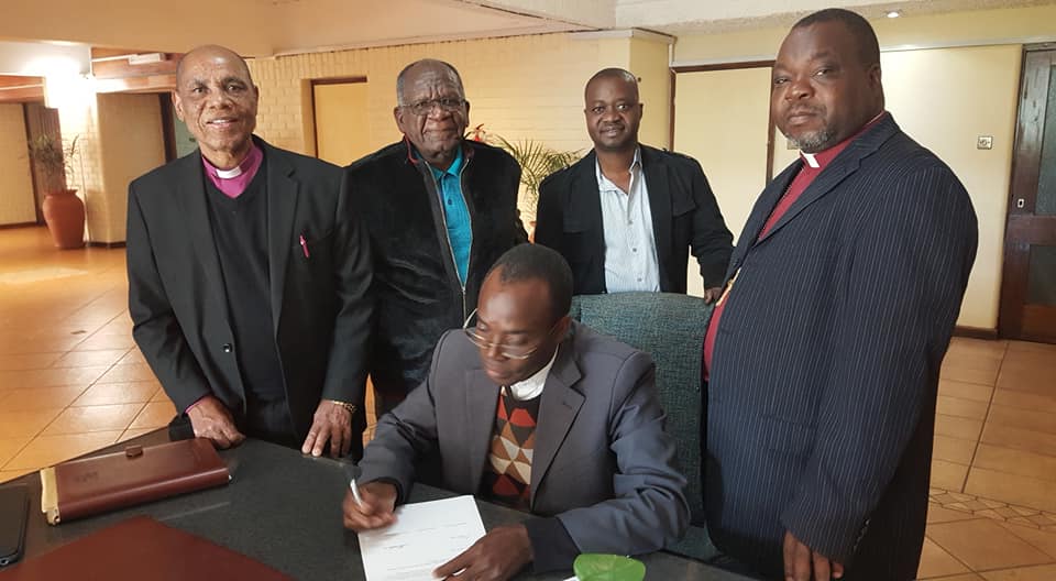 The Rev. Daniel Mhone signs an agreement aimed at ending a 10-year estrangement with another leader in the Malawi United Methodist Church. Shown, from left, are Zimbabwe Area Bishop Eben K. Nhiwatiwa, the Revs. Maxwell Jawati and Alfiado Zunguza and Anglican Bishop Gifford Matonga. Photo courtesy of Alfiado Zunguza.