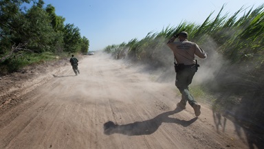 U.S. Border Patrol agents run down a dirt road amid swirling dust stirred up by a helicopter during a search for people who had crossed into the United States illegally and were hiding in heavily wooded areas and sugar cane fields near McAllen, Texas. Photo by Mike DuBose, UMNS. U.S. Border Patrol agents run down a dirt road amid swirling dust stirred up by a helicopter during a search for people who had crossed into the United States illegally and were hiding in heavily wooded areas and sugar cane fields near McAllen, Texas. Photo by Mike DuBose, UMNS.