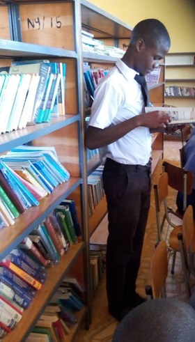 Takudzwa Musakwa (standing) studies a book in the new library at Nyanidzi Secondary School.  Photo by Kudzai Chingwe, UMNS.
