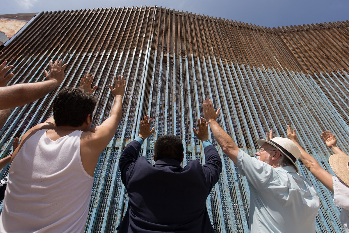 The Revs. Joel Hortiales (center, in blue blazer) and David Farley (to Hortiales' right) join parishioners of the Border Church in Tijuana, Mexico, as they lift their arms skyward beneath the fence that marks the border with the U.S. The Revs. Joel Hortiales (center, in blue blazer) and David Farley (to Hortiales' right) join parishioners of the Border Church in Tijuana, Mexico, as they lift their arms skyward beneath the fence that marks the border with the U.S.