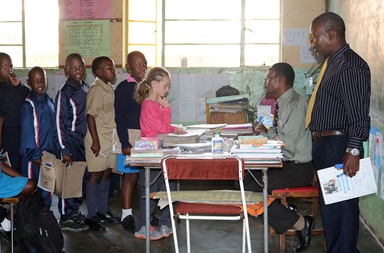 Mikayla Jaissle (center, wearing pink shirt) stands in line with other students while teacher Nicholas Chidzikwe checks her work at Hartzell Primary School in Mutare, Zimbabwe. The 10-year-old from Lakewood, Ohio, accompanied her mother, the Rev. Laura Jaissle, on the trip and attended class at the United Methodist school for two days. Photo by Eveline Chikwanah. Mikayla Jaissle (center, wearing pink shirt) stands in line with other students while teacher Nicholas Chidzikwe checks her work at Hartzell Primary School in Mutare, Zimbabwe. The 10-year-old from Lakewood, Ohio, accompanied her mother, the Rev. Laura Jaissle, on the trip and attended class at the United Methodist school for two days. Photo by Eveline Chikwanah.