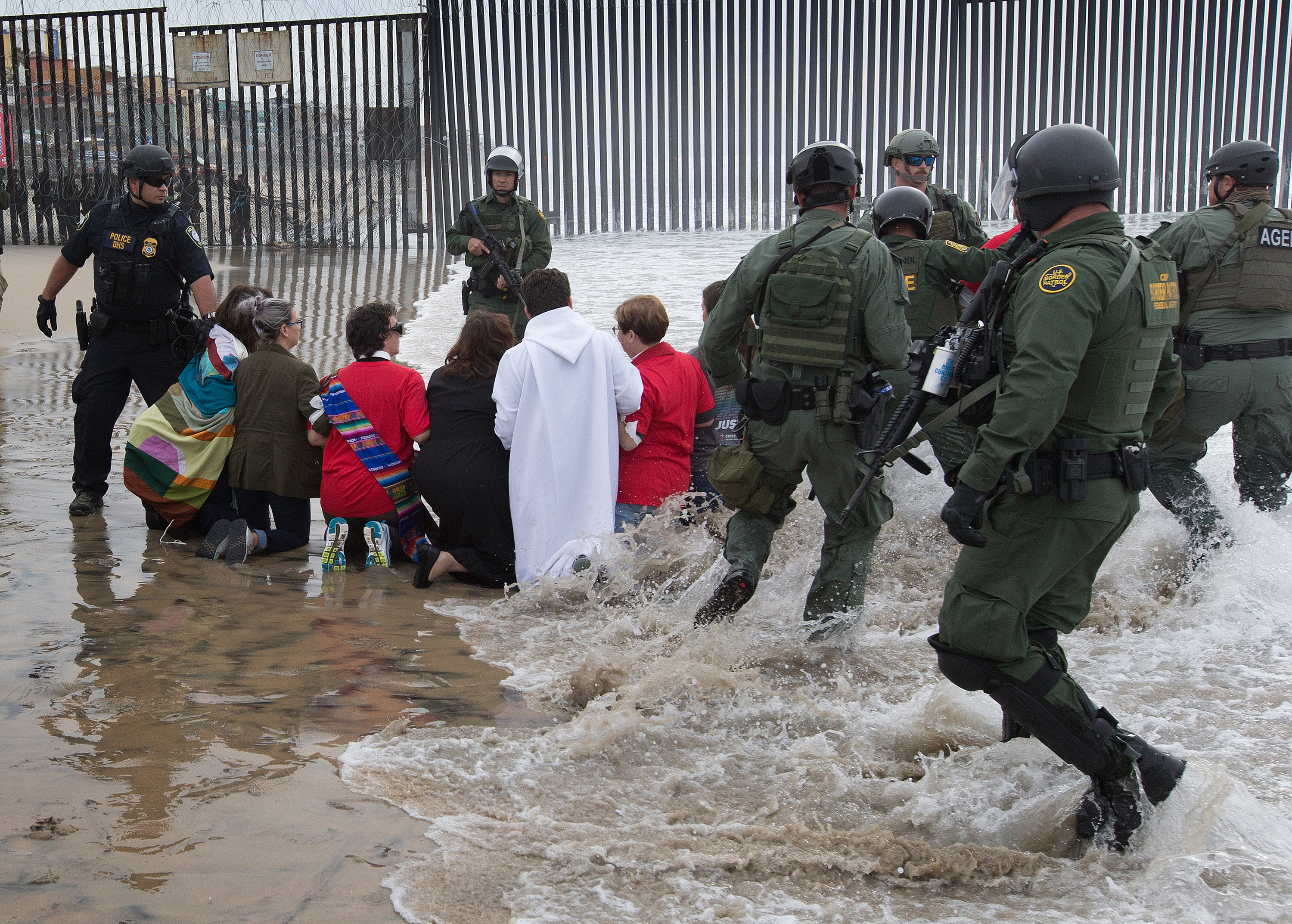 U.S. Border Patrol agents and officers from the Department of Homeland Security advance toward United Methodists leaders and organizers of a march calling for migrant justice as the marchers kneel on the beach at the fence between the U.S. and Mexico in San Diego.