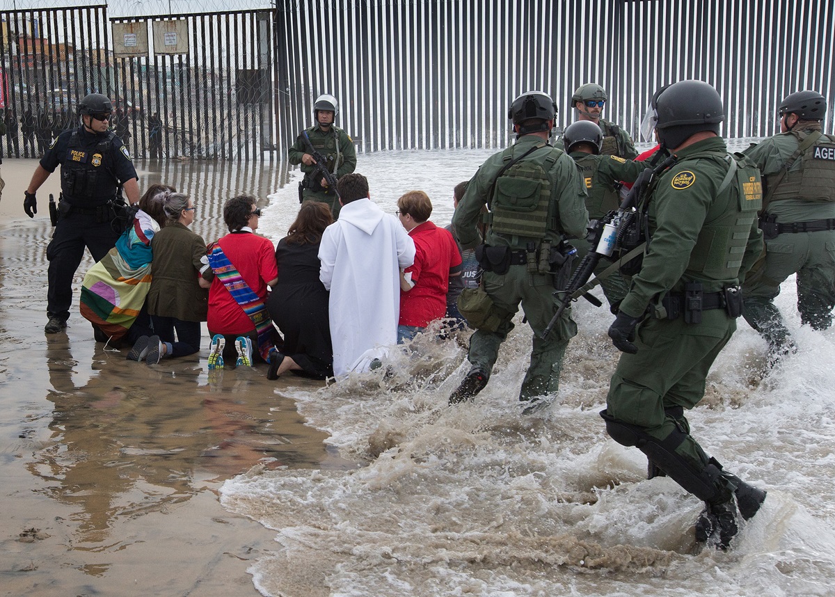 U.S. Border Patrol agents and officers from the Department of Homeland Security advance toward United Methodists leaders and organizers of a march calling for migrant justice as the marchers kneel on the beach at the fence between the U.S. and Mexico in San Diego. U.S. Border Patrol agents and officers from the Department of Homeland Security advance toward United Methodists leaders and organizers of a march calling for migrant justice as the marchers kneel on the beach at the fence between the U.S. and Mexico in San Diego.
