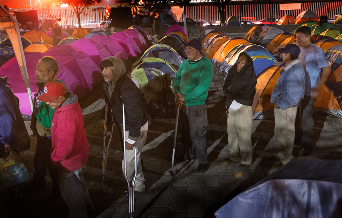 Residents of a makeshift camp at El Mapa Park in Tijuana, Mexico, line up for a meal provided by volunteers from the Methodist Church of Mexico and the Salvation Army. Many of the men are economic migrants from southern Mexico.