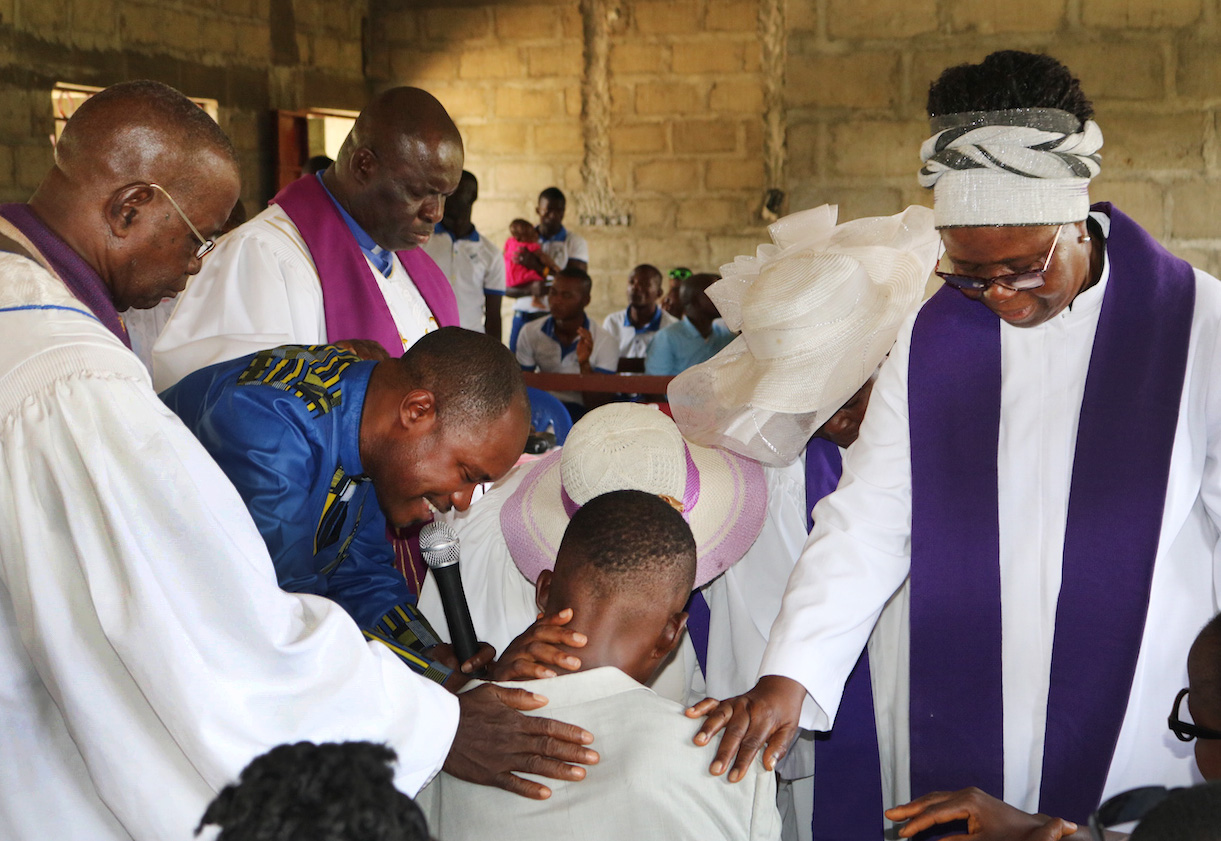 Visiting clergy from Freetown, Kenema and Kailahun, Sierra Leone, join the Rev. Judith Banya (standing right) to pray for Juana Jusu, who was partially paralyzed after an insect bite. Jusu traveled from Bomaru to join Baiwalla United Methodist Church  in celebrating its fifth anniversary. Photo by Phileas Jusu, UMNS.
