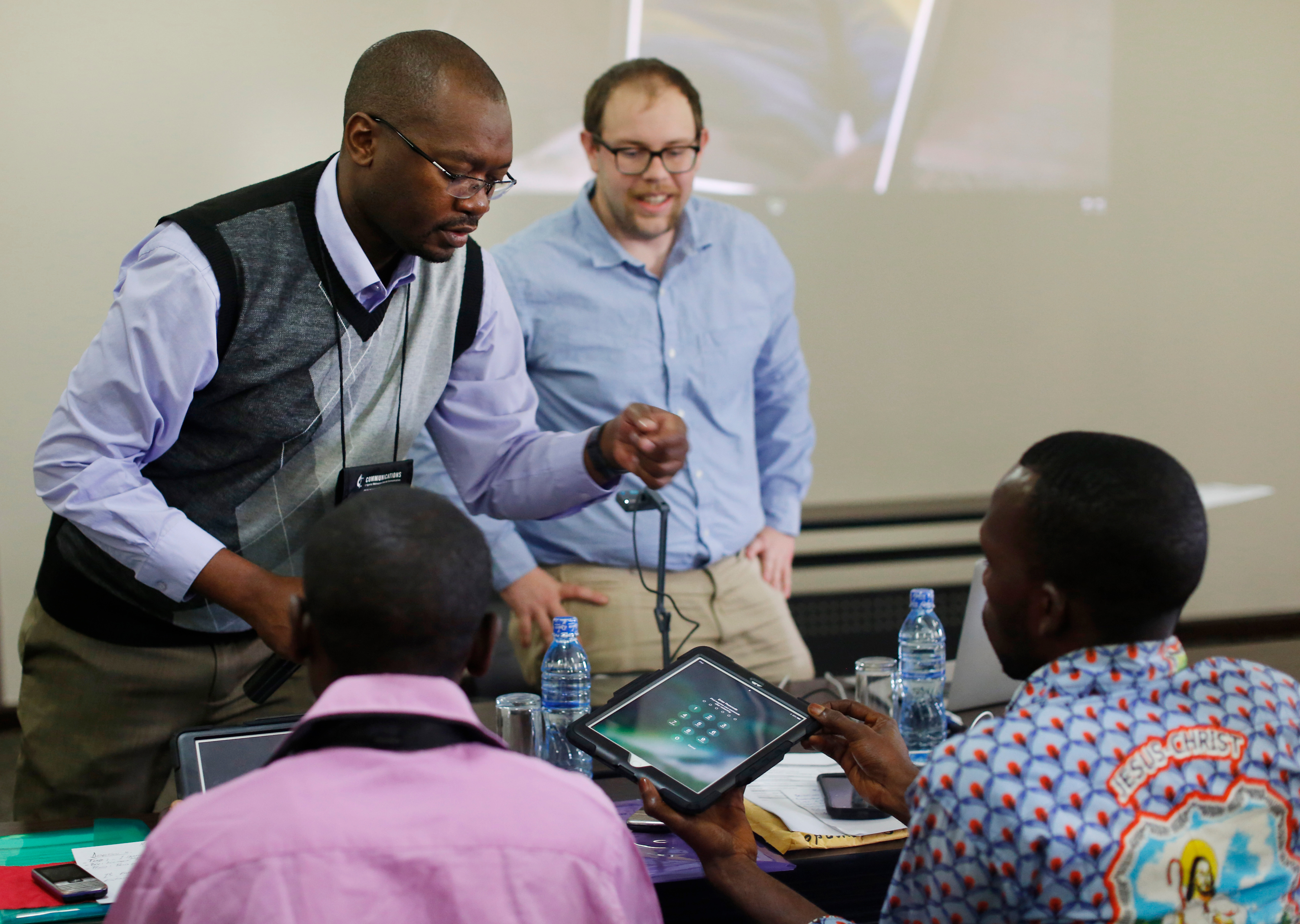 Chilima Karima and Matt Crum (standing) of United Methodist Communications instruct Roger Muzeze Tshinyemba and Francois Omanyondo Djonga in setting up their iPads during the training for Congo Central Conference communicators in Ndola, Zambia, in 2017. Agency leaders contend that a proposed 2021-24 budget cut of 37 percent is substantially more than for any other peer agency. File photo by Kathleen Barry, UMNS.