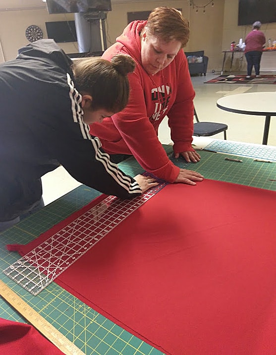 Red fabric is carefully measured as a first step in sewing a red shawl to honor murdered and missing indigenous women at Chemawa Indian Boarding School in Salem, Oregon. Photo by A. Wolf.