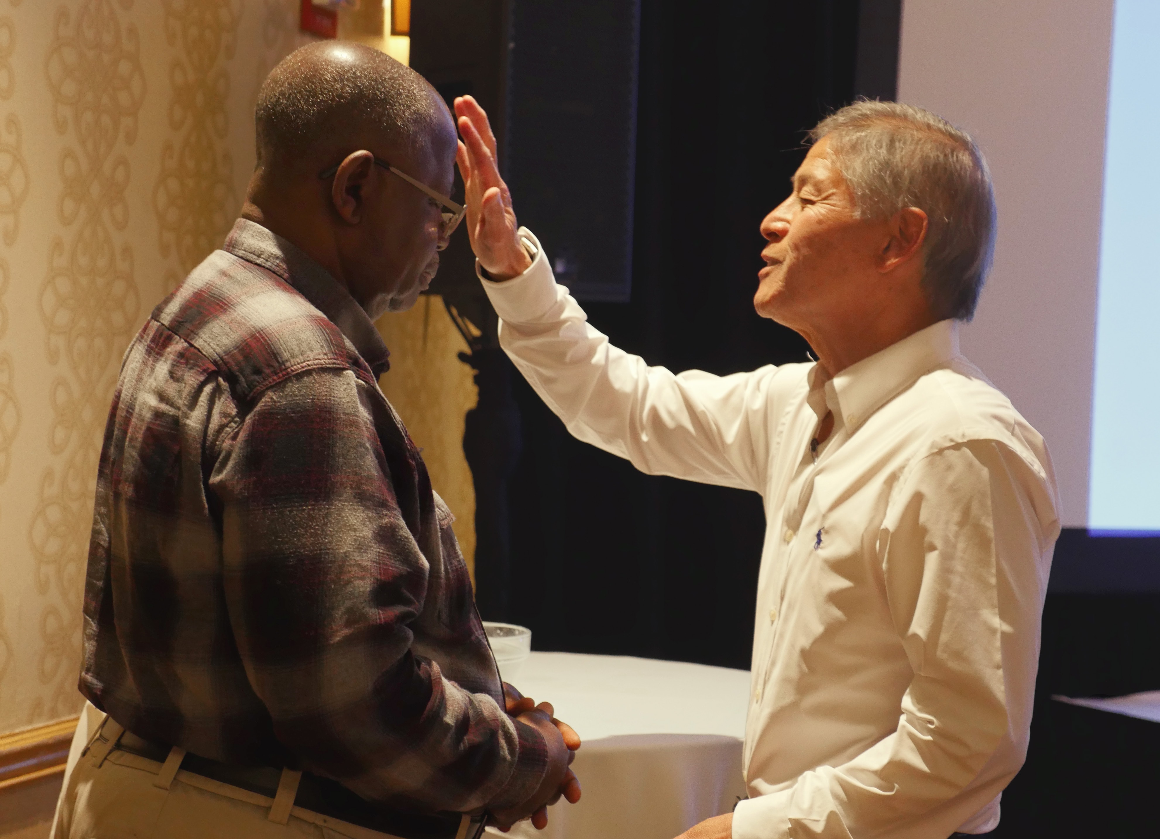 O Bispo Grant Hagiya, à direita, abençoa o Bispo aposentado David Yemba como parte da renovação dos votos de batismo dos bispos no final da reunião do Conselho dos Bispos da primavera. Hagiya lidera a Conferência California-Pacific e Yemba atua na República Democrática do Congo. Foto de Heather Hahn, Notícias MU.