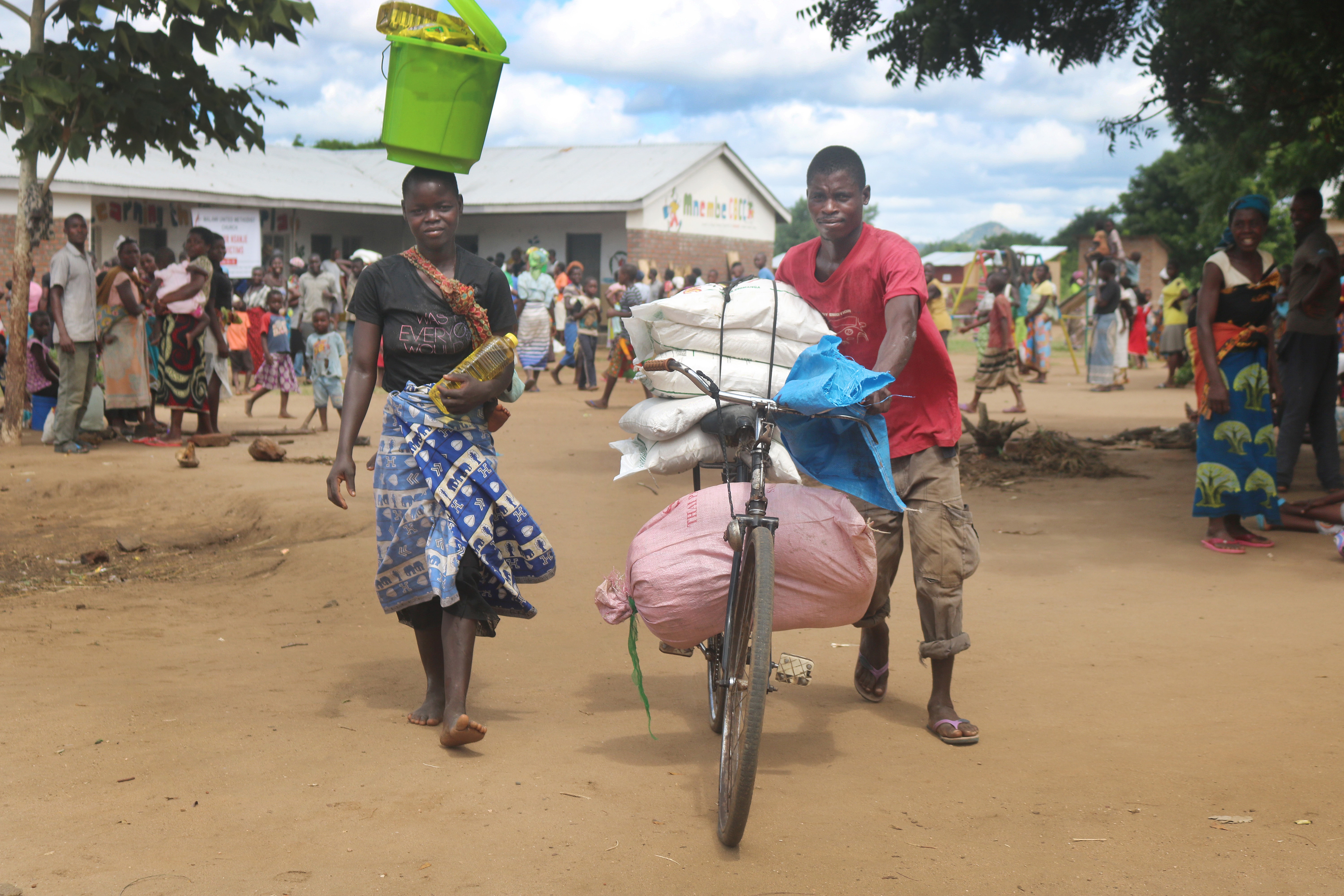 Shiku Kajalukapushes carries relief items received from the Malawi United Methodist Church on his bicycle. With him are his wife and baby. Photo by Francis Nkhoma, UM News.