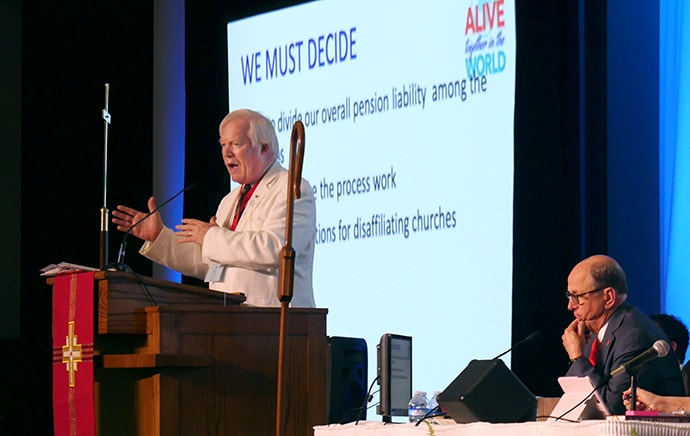 The Rev. Derek McAleer, South Georgia Conference treasurer and benefits officer, explains proposed annual conference policies on pensions and disaffiliation that augment what General Conference 2019 passed. He spoke during the 2019 South Georgia Annual Conference meeting in Columbus, Ga. Sitting beside him is Bishop R. Lawson Bryan. Photo by Heather Hahn, UM News.