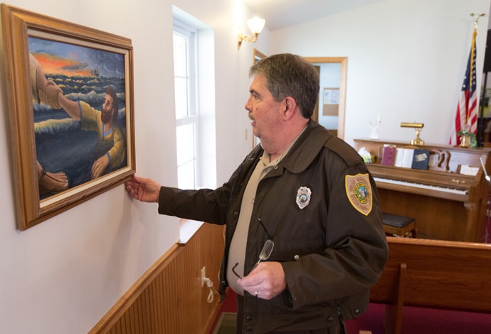 The Rev. Bradley Barton straightens a painting at Union Chapel United Methodist Church in St. George, W.Va. Barton is a correctional officer at the Tygart Valley Regional Jail in Belington and a licensed local pastor in The United Methodist Church. Photo by Mike DuBose, UMNS.