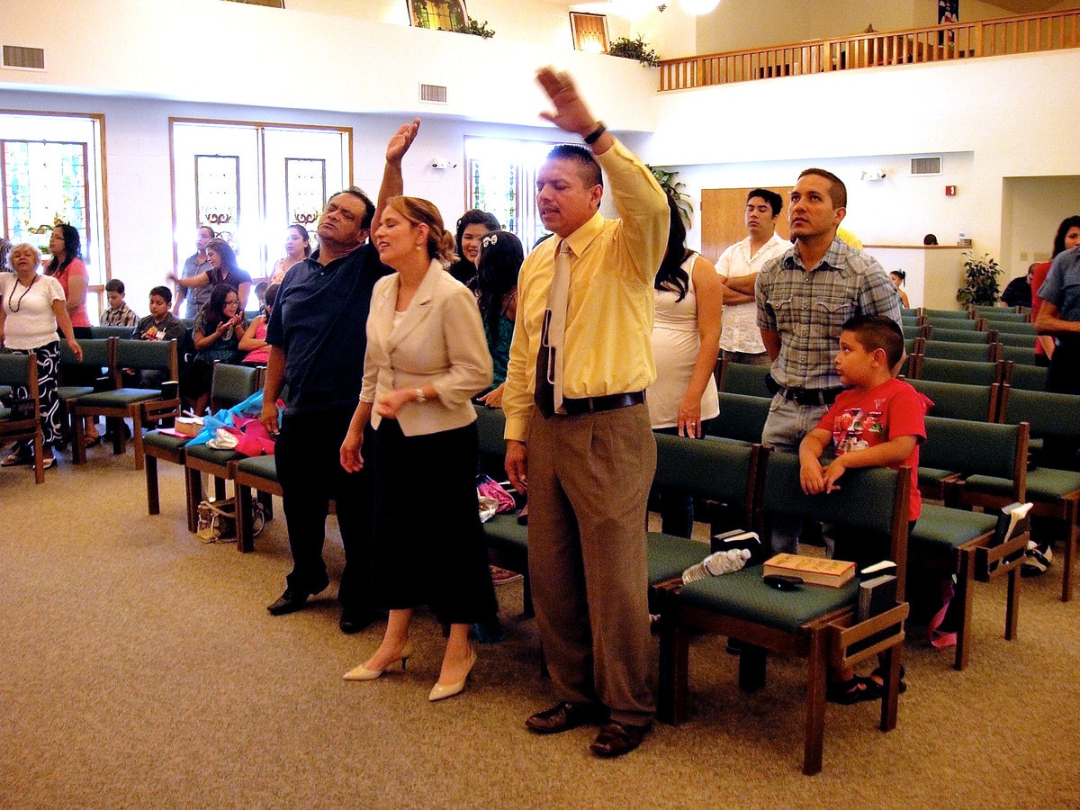 Lay missioner Ruben Rivera (hand raised in worship) prays with his wife, Julissa, at the La Luz de Cristo at Epworth United Methodist Church in Elgin, Ill. UMNS photo by J. Martin Lee.