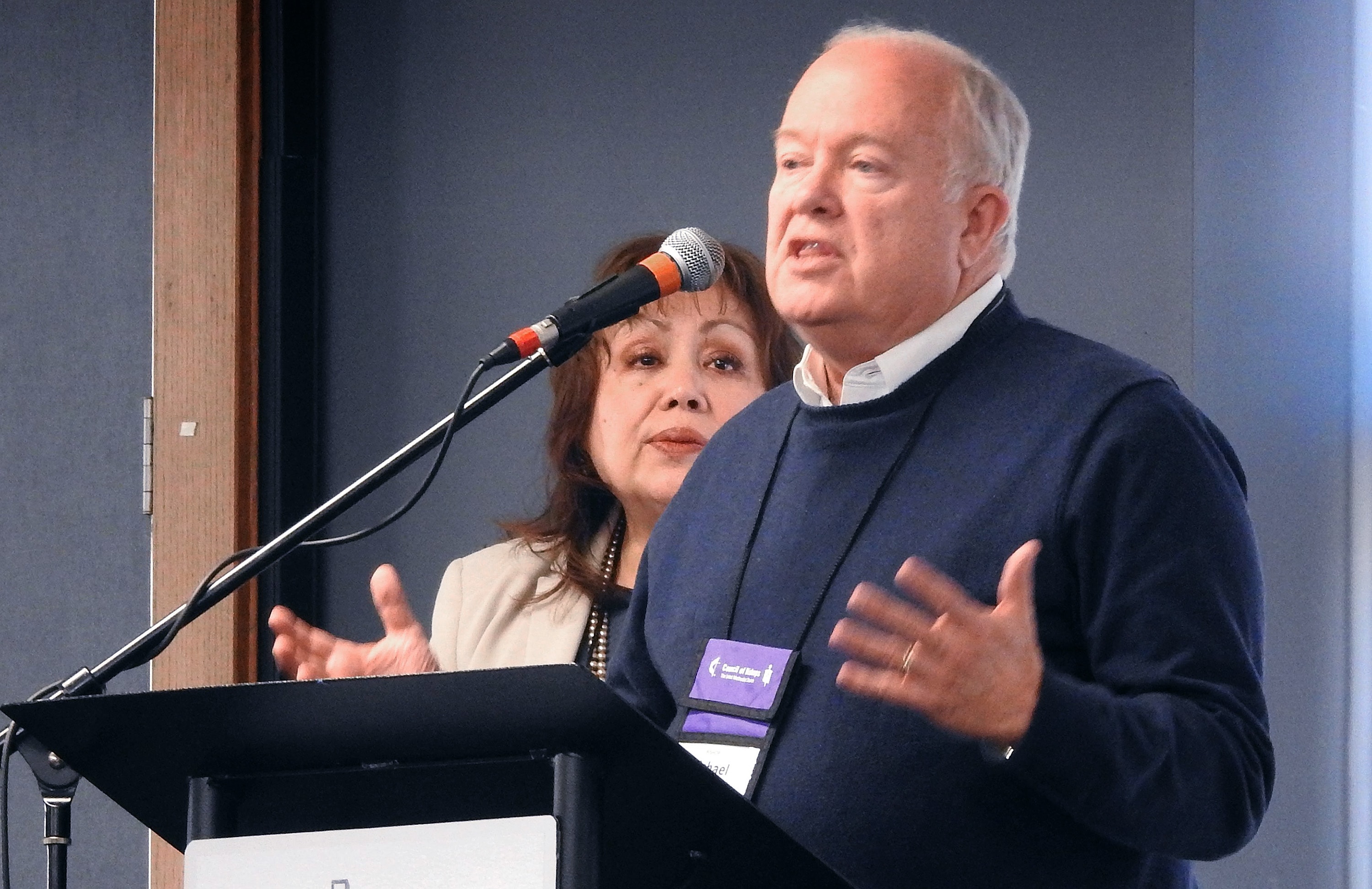 El Obispo Michael McKee, presidente del Concilio General de Finanzas y Administración (GCFA), habla durante la reunión del Concilio de Obispos/as en Lago Junaluska, Carolina del Norte, en la cual los/as lideres episcopales se enteraron que, al ritmo actual de ingresos por aportes, se quedarán sin fondos en 2024. En el podio lo acompaña la Obispa Minerva Carcaño. Foto por Sam Hodges, Noticias MU. 