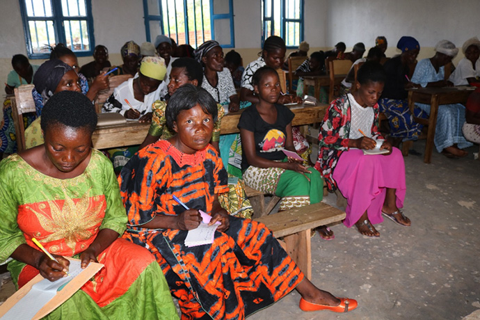 Helene Bataku (en robe orange), membre de l'église Méthodiste Unie Mwambangu à Fizi, a appris à lire et à écrire dans un nouveau centre de formation professionnelle dirigé par l'église Méthodiste Unie de Fizi, au Congo. Elle a déclaré que ce centre offrait aux femmes de nouvelles opportunités et une chance de rattraper leurs pairs. Photo de Philippe Kituka Lolonga, UM News.