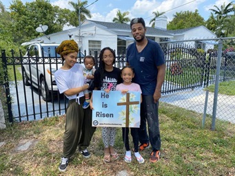 A family from First United Methodist Church of Miami stands with a yard sign given to them by the church. Photo by Kipp Nelson, First United Methodist Church of Miami. A family from First United Methodist Church of Miami stands with a yard sign given to them by the church. Photo by Kipp Nelson, First United Methodist Church of Miami.