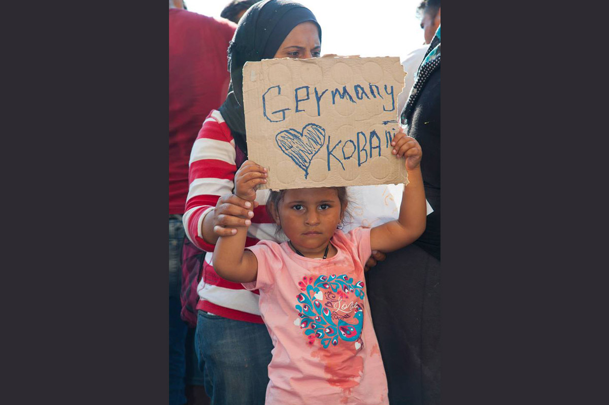 A young migrant girl hoping to reach Germany with her family holds up a sign inside the Hungarian border.  Photo by Oláh Gergely Máté.