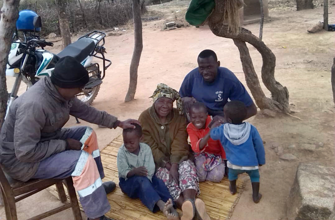 The Rev. Paul Nyagomo (left), pastor in charge of four United Methodist churches in the Marange District, visits with 79-year-old Agness Takodza in Mutare City, Zimbabwe, after delivering her medication. Seated with Takodza are her grandchildren, Nomsa (6) and Lessley (7), and Gift Takodza. Photo by Kudzai Chingwe, UM News. 