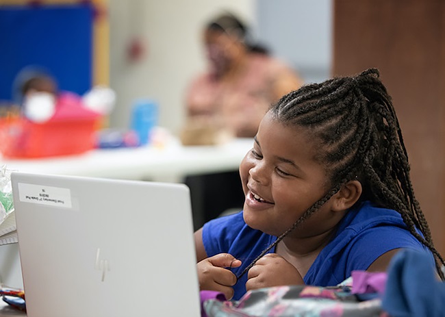 Una estudiante de primer grado interactúa con su maestro y compañeros/as de clase por computadora durante el primer día del programa Santuarios de Aprendizaje en la IMU Jones Memorial en Crestmont Park, Houston. Foto de Mike DuBose, Noticias MU.
