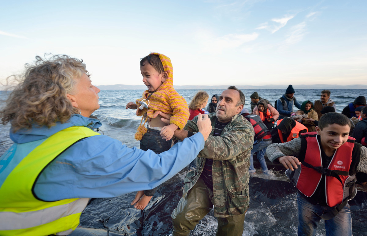 Voluntarios/as llevan a un niño a tierra en una playa cerca de Molyvos, en la isla griega de Lesbos, el 30 de octubre de 2015, después de que un grupo de refugiados/as cruzara el mar Egeo desde Turquía en un pequeño bote abarrotado de gente, proporcionado por traficantes turcos a quienes les habían pagado enormes sumas de dinero. Los/as refugiados/as fueron recibidos/as en Grecia por voluntarios/as locales e internacionales y luego se dirigieron hacia Europa occidental. Foto de archivo de Paul Jeffrey / Life on Earth Pictures. Voluntarios/as llevan a un niño a tierra en una playa cerca de Molyvos, en la isla griega de Lesbos, el 30 de octubre de 2015, después de que un grupo de refugiados/as cruzara el mar Egeo desde Turquía en un pequeño bote abarrotado de gente, proporcionado por traficantes turcos a quienes les habían pagado enormes sumas de dinero. Los/as refugiados/as fueron recibidos/as en Grecia por voluntarios/as locales e internacionales y luego se dirigieron hacia Europa occidental. Foto de archivo de Paul Jeffrey / Life on Earth Pictures.