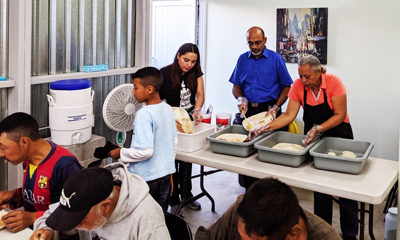 Roland Fernandes (al centro en la fila de atrás) trabaja con voluntarios/as mexicanos/as y estadounidenses en el Comedor Juan 6: 35, una cocina en Tijuana que proporciona comidas a los/as migrantes que llegan. Foto de Mia Nieves.
