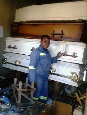 Fifteen-year-old Vanessa Chingwende stands beside finished coffins ready for sale in her workshop room near Marange, Zimbabwe. Photo by Chenayi Kumuterera, UM News.