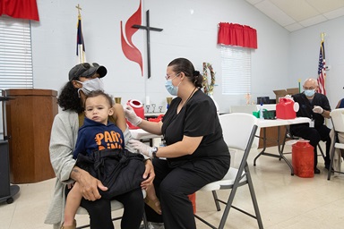 Camisha Henson sostiene a su hijo Welles en su regazo mientras recibe la vacuna COVID-19 de Tabitha England, RN, durante una clínica en la Iglesia Metodista Unida (IMU) San Marcos en Charlotte, Carolina del Norte. Camisha Henson sostiene a su hijo Welles en su regazo mientras recibe la vacuna COVID-19 de Tabitha England, RN, durante una clínica en la Iglesia Metodista Unida (IMU) San Marcos en Charlotte, Carolina del Norte.