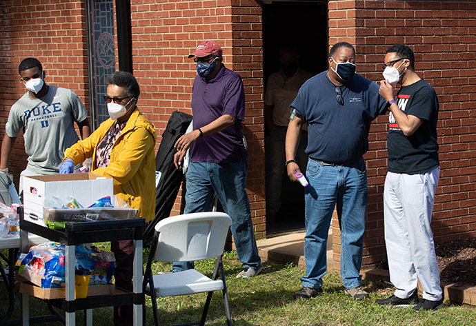 The Rev. Otto Harris (right) visits with church volunteer Andra Sutton outside St. Mark’s United Methodist Church in Charlotte, N.C., which was holding a COVID-19 vaccination clinic, while other volunteers prepared snack bags for vaccine recipients as they exited the church. From left are: Walter Hand III, Patricia Moore and André Dingle. Photo by Mike DuBose, UM News.