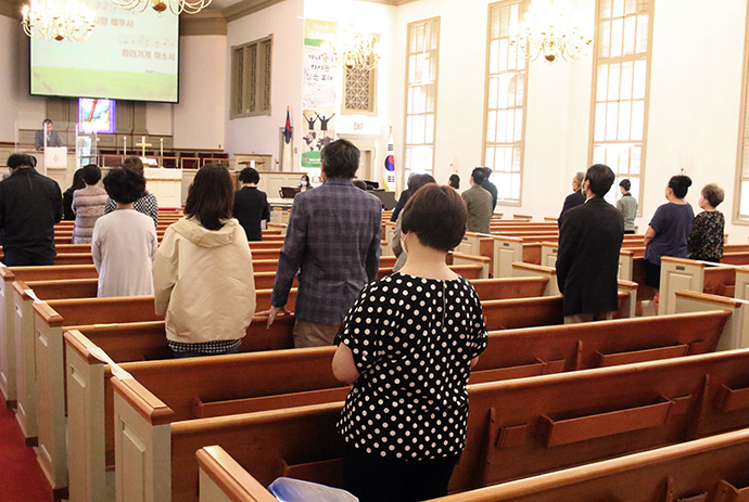 Members of Emmaus United Methodist Church worship together while following COVID-19 safety protocols in May. Members of the congregation wore face masks and practiced social distancing while a transparent screen stood in front of the altar. Photo by the Rev. Thomas Kim, UM News.